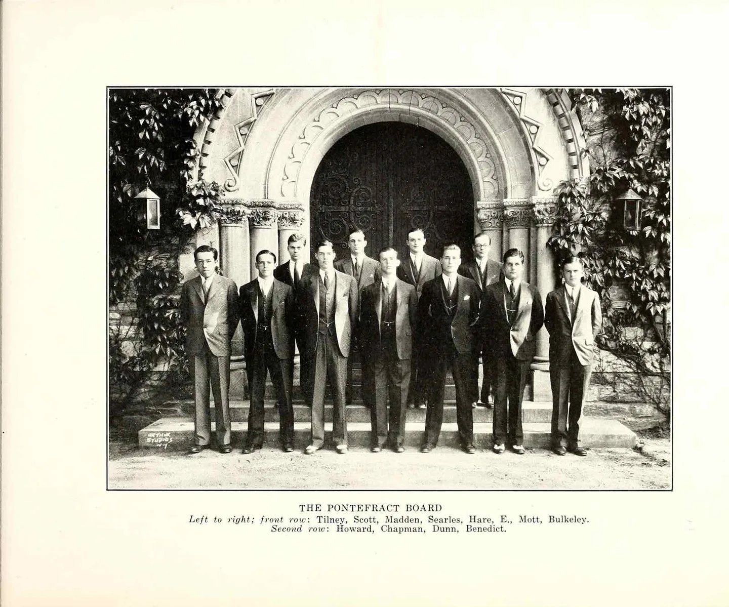 Eleven boys in 1930s suits stand in two rows on stone steps before the ivy-framed Romanesque arch of Clark Memorial Chapel's wooden doors; the printed caption below names them as The Pontefract board.